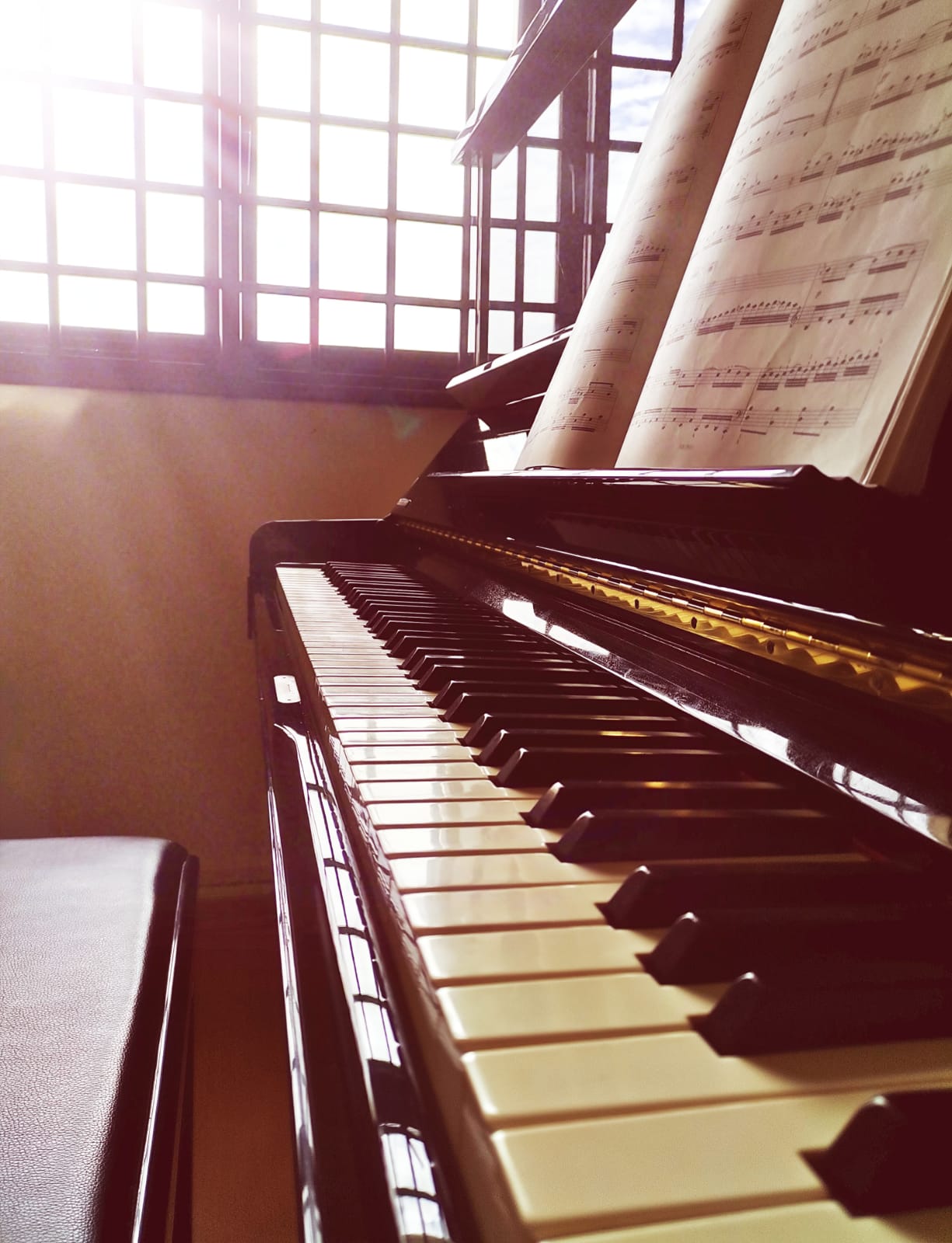 Side view of a piano beside a window with music books of the piano stand
